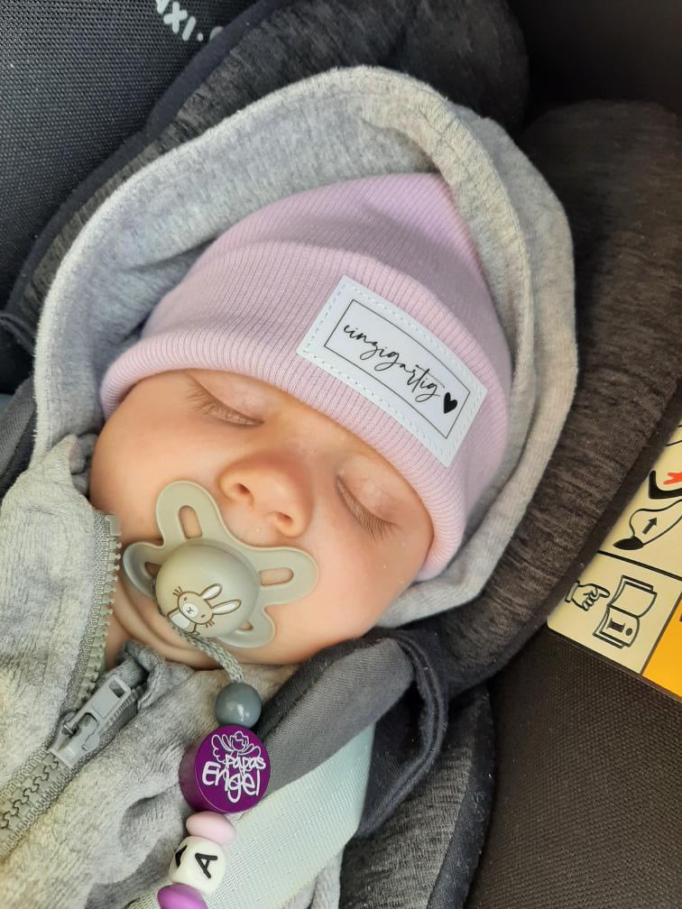 Schlafendes Neugeborenes mit fliederfarbener Beanie im Kinderwagen
