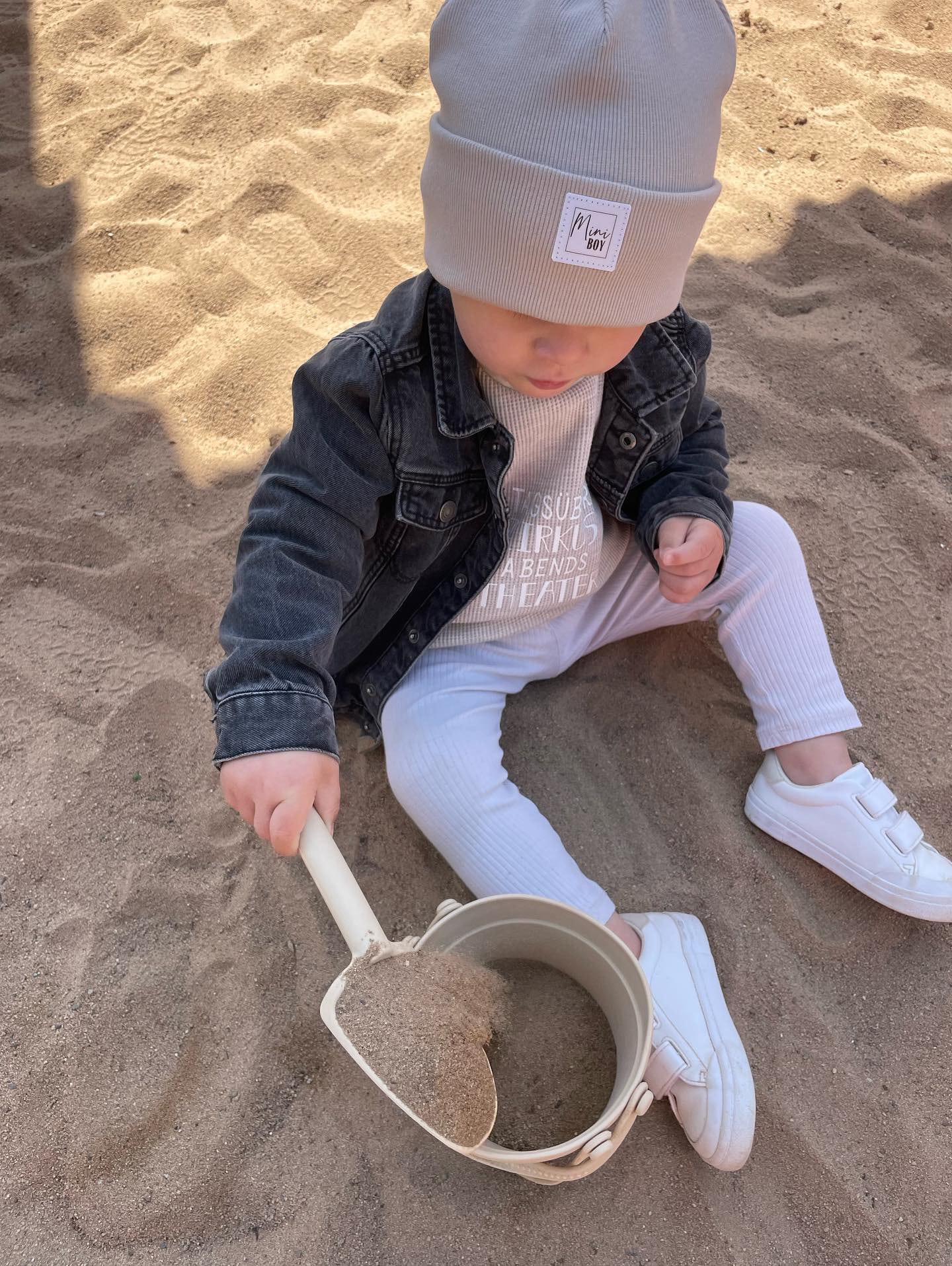 Kleiner Junge mit Beanie spielt im Sandkasten