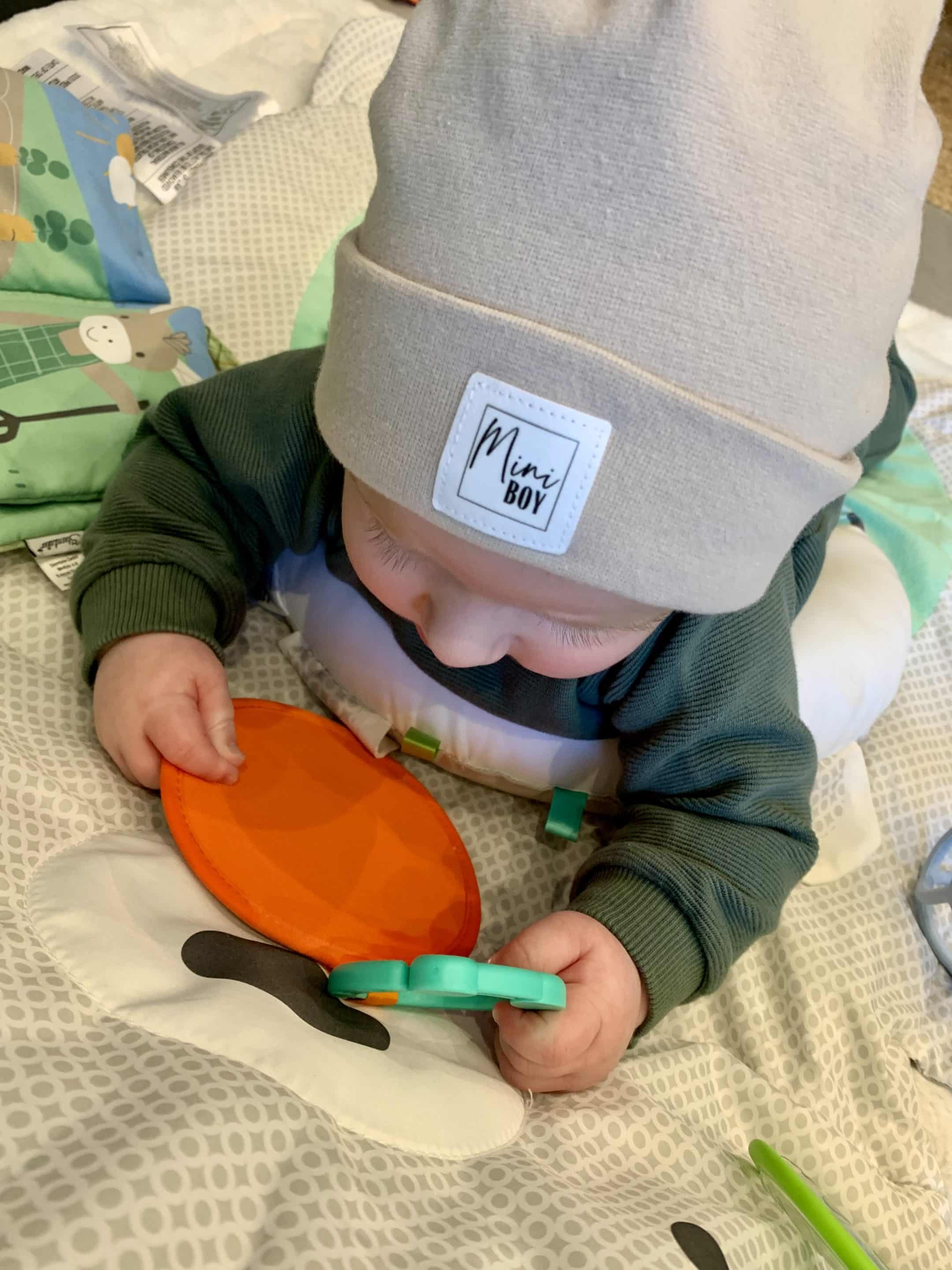 Kleiner Junge mit Unisex-Baby-Beanie spielt auf Spieldecke im Wohnzimmer